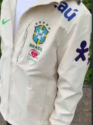 Vit Brasil Nike Gore-Tex jacka - Snygg vit träningsjacka från Nike med Brasilien CBF-logga, grönt Nike-märke och blåa detaljer. Jackan har dragkedja, huva och är tillverkad i slitstarkt Gore-Tex-material. Perfekt för sport eller streetwear och har flera sponsorloggor tryckta på bröst och ärm.