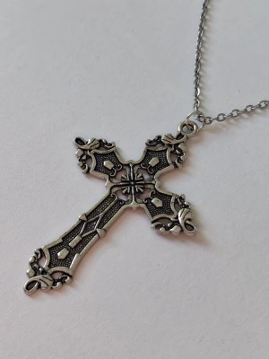 Kedjehalsband med kors i silverfärg - Snyggt halsband med ett detaljerat korshänge i antik silverfärg. Korset har fina ornament och mönster som ger en vintagekänsla. Kedjan är tunn och matchar hängets stil perfekt. Perfekt accessoar för dig som gillar unika smycken med karaktär. Materialet rostfritt stål. 