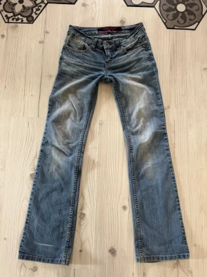 Blå bootcut jeans från Karve - Snygga blå bootcut jeans från Karve med klassisk femficksdesign och slitna detaljer. Jeansen har lågmidja, bälteshällor och dragkedjegylf. Perfekta för en avslappnad och trendig look. Mått: Midja 36 cm med lite stretch Innerben: 80 cm gren: 17cm