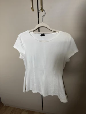 Vit basic t-shirt med rund hals - En enkel vit t-shirt med rund halsringning och korta ärmar. Modellen är klassisk och passar till det mesta. Tillverkad i mjukt bomullsmaterial för en skön känsla. Perfekt att matcha med jeans eller kjol.