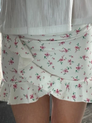 Vit blommig volangkjol - Supersöt kort kjol nu till sommaren. Är en liten fläck framtill, men inget man lägger märke till så mycket💕