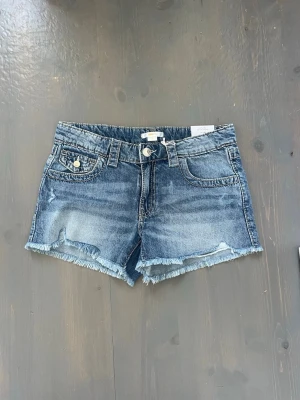 Blå jeansshorts - Snygga blå jeansshorts med fransig kant och slitningar framtill. Klassisk femficksmodell med knapp och dragkedja. Perfekta för varma dagar och enkel att matcha med allt. Jag skulle säga att de är lite stora i storleken. Pris kan diskuteras💕