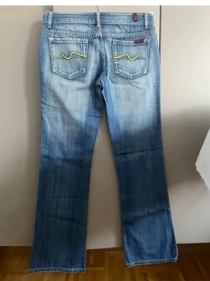 Blå  jeans från 7 for all mankind  - Snygga blå jeans fmed slitningar framtill och coola gula broderier på bakfickorna. Klassisk femficksmodell i denim med lätt tvättad look och låg midja. Perfekta för en avslappnad och trendig stil.