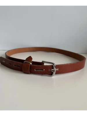 Brunt skärp i 100% äkta skinn med silverdetaljer - Stilrent brunt ÅL bälte / skärp i 100% äkta läder med ett klassiskt silverfärgat spänne. Bältet har flera hål för justering av storlek. 2,5cm brett och 118cm, passar midjemått mellan 96-115cm, motsvarande storlek M-XL. Fint skick!