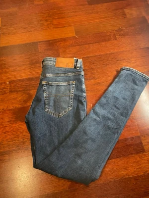 Mörkblå slim fit jeans - Snygga mörkblå slim fit jeans med klassisk femficksdesign och kontrastsömmar. Jeansen har en läderpatch i midjan och är tillverkade i ett stretchigt denimtyg som sitter tajt längs benen. Perfekta för en trendig och avslappnad look.