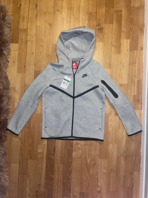 Grå Nike tech Hoddie - En grå snygg hoddie i märket Nike. Den är helt ny och oanvänd och säljs för att den var för stor.