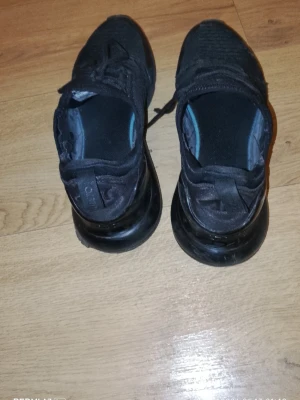 Svarta Nike Air Max 270 sneakers - Säljer ett par helsvarta Nike Air Max 270 sneakers med stickad ovandel och synlig Air Max-dämpning i hälen. Skorna har klassisk snörning och sportig design, perfekt för dig som gillar streetwear och bekväma sneakers.