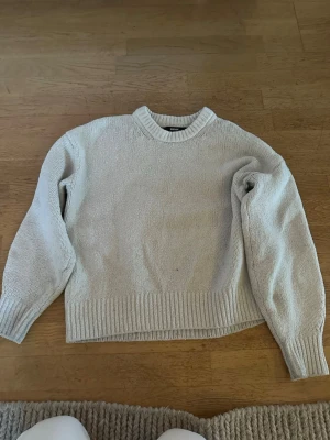 Ljusgrå stickad tröja från BikBok - Ljusgrå stickad tröja från BikBok med rund halsringning och ribbade muddar vid ärmslut och nederkant. Tröjan har en klassisk, rak passform och är perfekt för lager-på-lager-stil under kyliga dagar.