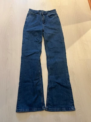 Blå utsvängda jeans från Indiska - Snygga blå jeans från Indiska i modell med utsvängda ben. Klassisk femficksdesign och hög midja. Perfekta för dig som gillar en retroinspirerad look. Tillverkade i denim med en skön passform.
