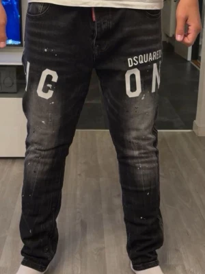 Svarta Dsquared2 ICON jeans - Snygga svarta jeans från Dsquared2 med vit 'ICON'-text framtill. Jeansen har en slim fit-modell, slitna detaljer och blekta partier för en cool streetstyle-look. Klassisk femficksdesign och knappgylf. Perfekta för dig som gillar trendiga och unika jeans.