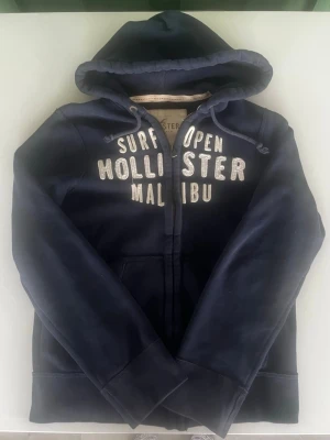 Hollister Malibu California surf hoodie mörkblå - Riktigt snygg och eftertraktad Hollister Malibu surf hoodie. fint skick inga fel storlek M kan ta mått vid behov. Endast 415kt ej hugget i sten kom gärna med frågor och prisförslag har även mycket mer liknande i min profil alla storlekar kolla gärna stor rabatt vid köp av flera 😁✌️