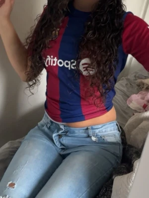 Barça tröja i blått och vinrött - Säljer en FC Barcelona matchtröja i klassiska blå och vinröda ränder med klubbmärke och sponsorlogga på bröstet. Tröjan har korta ärmar och rund hals, perfekt för fotboll eller träning.