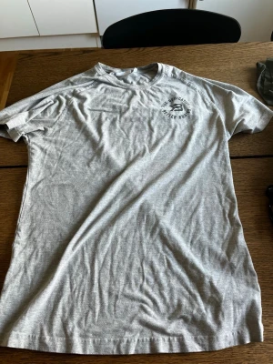Grå t-shirt med tryck från Better Bodies - Snygg grå t-shirt från Better Bodies med litet svart tryck på bröstet. Klassisk rund halsringning och korta ärmar. Perfekt för en avslappnad stil eller till gymmet.