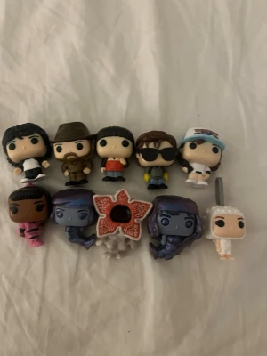 Stranger Things Funko Pop minifigurer - Samling med tio små Funko Pop minifigurer från Stranger Things. Figurerna är färgglada och föreställer olika karaktärer från serien, inklusive både människor och monster. Perfekt för fans av serien eller som dekoration till hyllan.