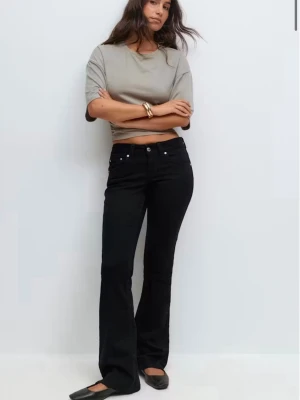 Svarta bootcut jeans med fickdetaljer - Säljer ett par svarta bootcut jeans med snygga fickor bak som har lock och silverfärgade knappar. Jeansen har klassisk femficksdesign och bälteshällor. Perfekta för dig som gillar en tidlös och clean look.