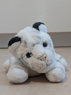 Vit mjukistiger med svarta detaljer - Söt mjukistiger i vitt plyschmaterial med svarta detaljer på öronen och runt ögonen. Har broderad nos och svarta plastögon. Perfekt som gosedjur eller dekoration i rummet. Längd ca 20 cm