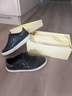 Svarta Axel Arigato sneakers - Snygga svarta sneakers från Axel Arigato med vit sula och diskret logga på sidan. Skorna har klassisk låg profil och är tillverkade i läder med svarta skosnören. Levereras med originalkartong och dustbag. Skorna är i väldigt bra skick och kommer även med oanvända sulor.