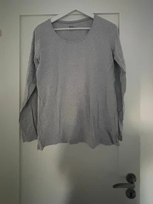 Grå långärmad topp från Basic - En enkel och stilren grå långärmad topp från Basic. Tillverkad i mjuk bomull med rund halsringning och normal passform. Perfekt att matcha med jeans eller kjol för en clean look.