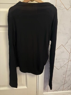 Svart långärmad tröja basic - En enkel svart långärmad tröja med rund hals. Tröjan har en tajt passform och är tillverkad i ett tunt, mjukt material som känns skönt mot huden. Perfekt att matcha med jeans eller kjol för en clean look.
