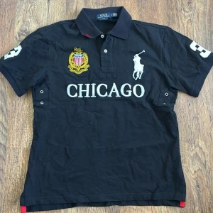 Svart Chief Keef ”Chicago” Polo Ralph Lauren - (OBS Står stlk L men passar mer som M, lapp bortklippt för ökad comfort!) Svart pikétröja från Polo Ralph Lauren med broderad logga och texten CHICAGO på bröstet. Tröjan har krage, knappar vid halsen och vita detaljer på ärmarna. Tillverkad i bomull och har en klassisk, sportig look.