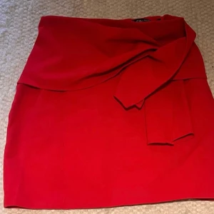 Röd omlottkjol från Zara - Snygg röd omlottkjol från Zara med ”knyt” i midjan. Kjolen har en kort och figurnära passform som ger en trendig look. Perfekt för dig som vill sticka ut med en färgstark och modern stil.
