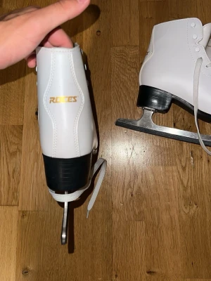 Vita konståkningsskridskor Roces - Snygga vita konståkningsskridskor från Roces med klassisk design. Skridskorna har högt skaft, vita snören och svart sula samt klack. Bladen är i metall och skon är tillverkad i syntetmaterial. Perfekta för isbanan eller träning.