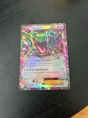 Rayquaza EX Pokémonkort holografiskt - Säljer ett Rayquaza EX Pokémonkort med holografisk yta. Kortet har färgstark design med Rayquaza i grönt, rött och gult mot en glittrig bakgrund. Perfekt för samlare eller Pokémonfans som vill utöka sin kortsamling.