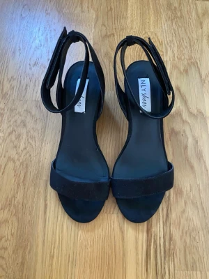 Svarta sandaletter med blockklack  - Superfina och stilrena svarta sandaletter i mockaimitation från NLY Shoes (Nelly). Skorna har en stadig och bekväm blockklack, en bred rem över tårna samt en justerbar rem runt ankeln för perfekt passform. Modellen är designad med en snygg öppen häl vilket ger en väldigt luftig och modern känsla * Märke: NLY Shoes (Nelly) * Storlek: 37 (Innermått: Ca 24 cm) * Skick: Mycket bra skick (Endast använda vid ett enstaka tillfälle, se bilder för detaljer) * Klackhöjd: Ca 6 cm (Stabil blockklack) * Mate