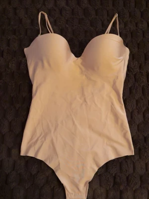 Beige-rosa body med tunna axelband - Beigerosa body med tunna justerbara axelband och vadderade kupor. Snygg när man är brun. Köpt på plick