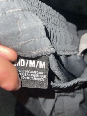 Grå cargobyxor från Under Armour - Snygga grå cargobyxor från Under Armour med elastisk midja och praktiska fickor med dragkedja på sidan. Tillverkade i ett lätt och flexibelt material som ger skön passform. Perfekta för en aktiv vardag och streetwear-stil.