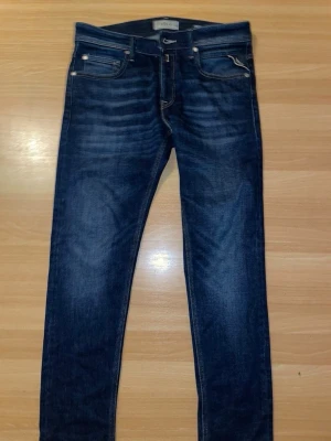 Replay Jeans - Snygga mörkblå slim fit jeans med klassisk femficksdesign och diskreta slitningar framtill. Jeansen har kontrastsömmar och en bakficka med dekorativ söm. Perfekta till en avslappnad streetstyle-look. STORLEK W28 L30