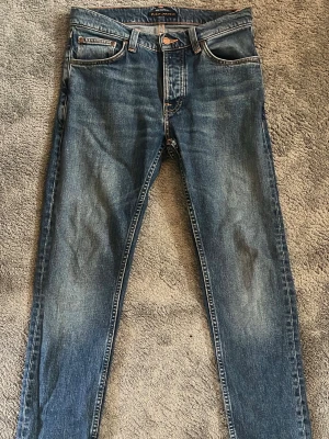 Nudie Jeans Blå  W28 L32 - Snygga blå slim fit jeans från Nudie. Jeansen har normal midja, dragkedjegylf och är tillverkade i bomull med lite stretch för extra komfort. Perfekta för en avslappnad och trendig look. Extremt snygga. Storlek 28w 32L