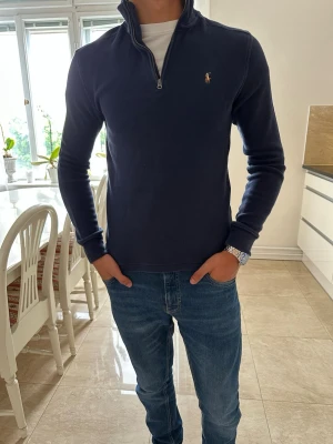 Mörkblå quarter zip från Ralph Lauren - Mörkblå långärmad tröja från Ralph Lauren med quarter zip och liten broderad logga på bröstet. Tröjan har hög krage och är tillverkad i mjukt material som passar perfekt till jeans. Enkel och stilren design som funkar till många olika looks.