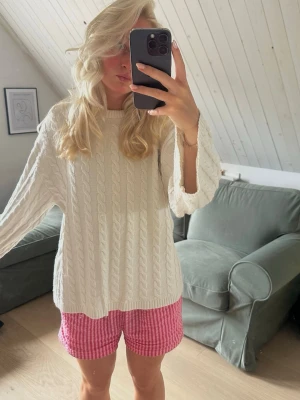 Vit kabelstickad tröja - Säljer en oversized vit kabelstickad tröja med rund hals och långa ärmar. Tröjan har ett klassiskt flätmönster och är perfekt för lager på lager. Materialet ser mjukt och mysigt ut, perfekt för kyligare dagar.