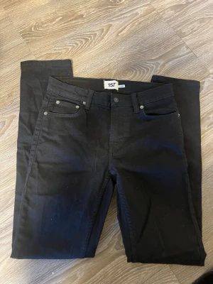 Svarta jeans från 157 - Snygga svarta jeans från 157 med klassisk femficksmodell och raka ben. Jeansen har bälteshällor och knappgylf. Perfekta för en stilren och enkel look. Materialet känns mjukt och följsamt, vilket gör dem bekväma att bära hela dagen.