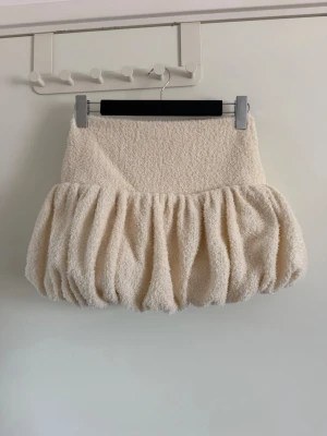 Beige volangkjol i frotté - Supersöt beige kortkjol med volang och ballongformad siluett. Kjolen är gjord i mjuk frotté och har en bred midjeresår som ger en bekväm passform. Perfekt för dig som vill sticka ut med en unik och fluffig look. Använd en gång.