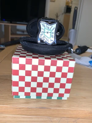 Laphton. square melting  - Har haft den på mig i 2 veckor har börjat med löpning och träning använder istället nu Apple Watch dagligen den har nu bara legat senaste 4 månader hemma därför vill jag sälja den allt funkar med den som det ska inga skador eller repor Säljer en unik klocka inspirerad av Salvador Dalí med böjd, silverfärgad urtavla och romerska siffror. Klockan har ett svart band i skinn med struktur och klassiskt spänne. Perfekt för dig som gillar konstnärliga accessoarer.    