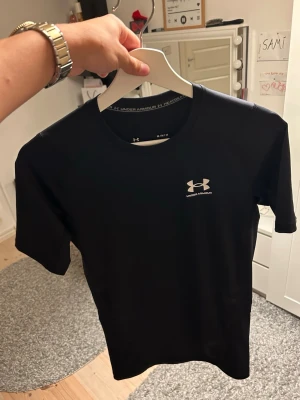 Compression shirt från Under Armour - Snygg svart compression shirt från Under Armour med korta ärmar och rund hals. Tillverkad i ett lätt och snabbtorkande funktionsmaterial, perfekt för gymmet eller löprundan. Diskret logga på bröstet och nacken för en sportig look. Slim fit och perfekt för dig som gillar att gymma och kollar mycket gym tiktoks. Storlek M