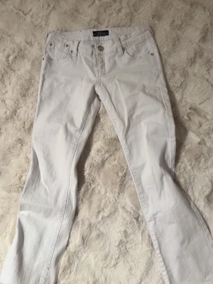 Vita bootcut jeans från Madonna  - Säljer ett par vita bootcut jeans från Madonna. Klassisk femficksmodell med en låg midja och snygg passform. Jeansen är i ett mjukt denimtyg och har silverfärgade knappar. Jag köpte dessa jeans men har inte använt dem, därför väljer jag att sälja dem istället så de kan hamna hos en människa som faktiskt kommer använda dem istället. Pris kan diskuteras 