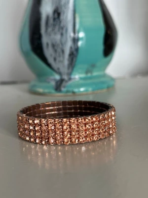 Bredt armband med roséguldiga pärlor - Snyggt och brett armband med flera rader glittrande roséguldiga pärlor. Armbandet är elastiskt och täckt av små, tätt sittande pärlor som ger en lyxig och trendig känsla. Perfekt accessoar för att lyfta vilken outfit som helst.