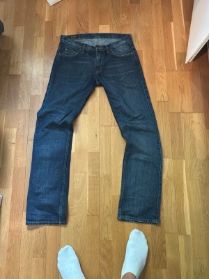 Mörkblå raka jeans från Lee - Säljer ett par klassiska mörkblå jeans från Lee med rak passform. Jeansen har fem fickor, gylf med dragkedja och knapp samt diskreta slitningar för en avslappnad look. Tillverkade i slitstark denim som passar perfekt till vardagsstilen.
