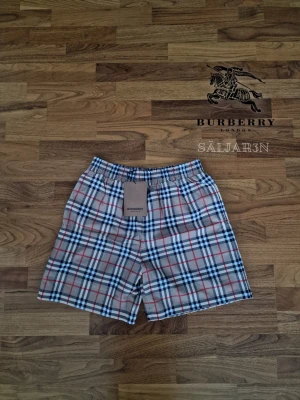 Burberry Shorts - Letar du efter lyxiga badshorts med stil? Dessa helt nya Burberry-shorts i klassiska rutor kombinerar sofistikerad design med hög komfort. Tillverkade i kvalitativ bomull med mesh-innershorts och elastisk midja för perfekt passform. Originaletikett "BURBERRY London England" kvar. Perfekta för strand, pool eller semester!  Storlek L passar M | Skick: Nya med taggar | 📦 Snabb leverans!  Hör av dig vid intresse eller funderingar!.