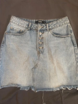 Ljusblå jeanskjol från Bik Bok - Trendig ljusblå jeanskjol från Bik Bok med rå kant nertill. Perfekt till en avslappnad och cool stil.