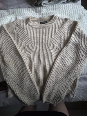 Beige stickad tröja - Säljer en beige stickad tröja från XOXO friends. Tröjan har ett snyggt ribbstickat mönster med detaljer längs ärmar och bröst, rund halsringning och långa ärmar. Perfekt för lager på lager och riktigt mysig till hösten.