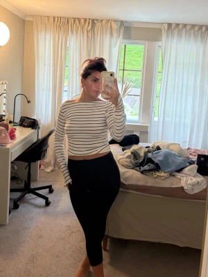 Randig croppad långärmad topp - Säljer en vit croppad topp med svarta horisontella ränder. Toppen har långa ärmar och en något lös passform. Perfekt för dig som gillar en enkel men stilren look. Materialet känns mjukt och stretchigt, troligen bomull eller en bomullsblandning.