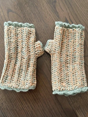 Virkade fingerlösa vantar i orange och grön - Unika handstickade fingerlösa vantar i orange och ljusgrön. Vantarna har ett ribbat mönster och vågig kant upptill och nedtill. Perfekta för dig som vill ha värme men ändå kunna använda mobilen.