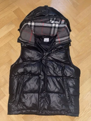 Svart dunväst från Burberry - Säljer min svarata burberry jacka då den är för liten den är varm och snygg dock fattas de några knappar på den och det finns ett litet hål på sidan men de är inget man tänker på annars väldigt snygg skriv för fler frågor 