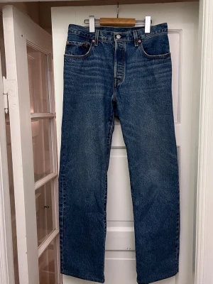 Levi's raka blå jeans - Klassiska 501or, blå jeans från Levi's med rak passform och fem fickor. Jeansen har en djupblå tvätt med subtila slitningar och kontrastsömmar. Tillverkade i kraftig denim med knappgylf och ikonisk läderpatch bak i midjan.
