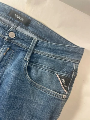 Replay Anbass blå jeans slim fit - Säljer ett par snygga Replay Anbass jeans i klassisk blå tvätt. Modellen är slim fit med normal passform och raka ben. Jeansen har fem fickor, tydliga sömmar och Replay-logga på fickan. Materialet är slitstarkt jeans i bomull med lite stretch för extra komfort.