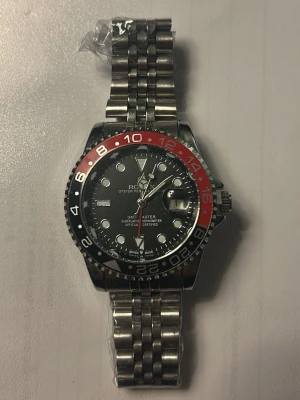  GMT-Master II klocka silver/röd -   GMT-Master II med klassisk tvåfärgad vridring i svart och rött. Klockan har en robust länk i silverfärgat stål och tydliga index på svart urtavla. Perfekt för dig som gillar stilrena accessoarer med ikonisk design.